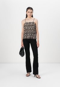 Camisola s uzorkom životinja s volanima, nosi se s crnim širokim hlačama. Model drži malu crnu torbicu; minimalistička pozadina.