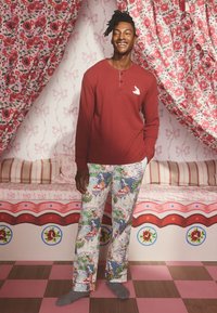 Czerwona koszula z długim rękawem z małym białym nadrukiem na piersi, zestawiona z kolorowymi spodniami do piżamy w wzory z fantazyjnymi motywami.