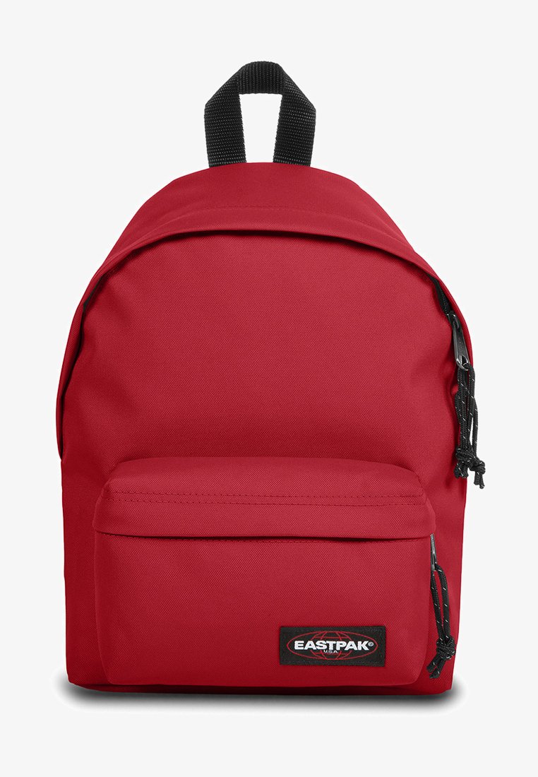 Red fabric backpack with a smooth texture, featuring a front zipper pocket, adjustable straps, and a top carry handle. Logo patch displayed.