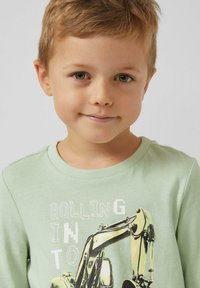 Jasnozielona bawełniana koszulka z nadrukiem pojazdu budowlanego i napisem, o okrągłym dekolcie i prążkowanym obszyciu kołnierza.