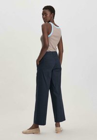 Beige top tankki vaaleansinisellä reunuksella, yhdistettynä laivastonsinisiin leveälahkeisiin housuihin, joissa on taskut. Malli seisoo kädet taskuissa, jalassa beiget ballerinat.