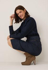 Denim dress with a fitted silhouette, dark wash, long sleeves, and a collar. Paired with high-heeled, sock-style brown boots.