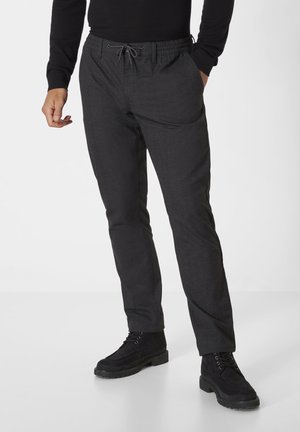 Black pants with a textured fabric, featuring an elastic waistband, adjustable drawstring, and side pockets. Worn with black ankle boots.