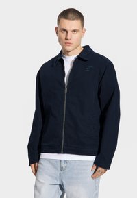 Granatowa kurtka zapinana na zamek z kołnierzykiem, długimi rękawami i bocznymi kieszeniami; charakteryzuje się subtelnym logo na klatce piersiowej oraz gładką teksturą.