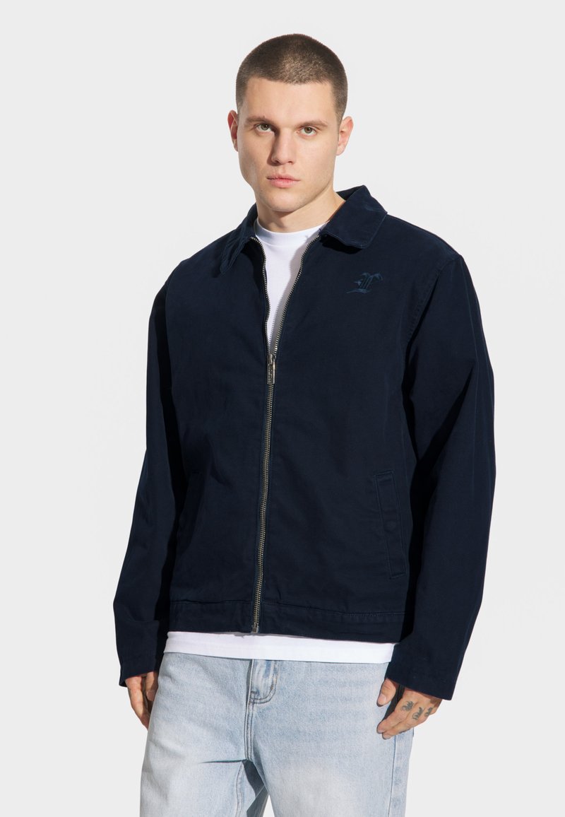 Granatowa kurtka zapinana na zamek z kołnierzykiem, długimi rękawami i bocznymi kieszeniami; charakteryzuje się subtelnym logo na klatce piersiowej oraz gładką teksturą.