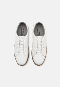 White leather sneakers with a smooth finish, featuring a low-top design, round toe, six eyelets, and brown rubber soles.