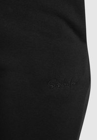 Zwarte sweatpants met een gladde textuur beschikken over een subtiel geborduurd logo aan de zijkant. Het ontwerp is eenvoudig en taps toelopend.