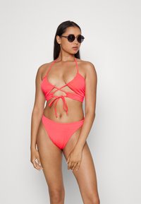 Conjunto de biquíni em coral, apresentando um top com laço à frente e alças cruzadas, e calções de cintura alta. Tecido suave e elástico com cobertura mínima.