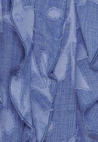 Blåt stof med teksturerede, uregelmæssigt syede mønstre og bløde, bølgede folder, der skaber en lagdelt, taktil overflade.