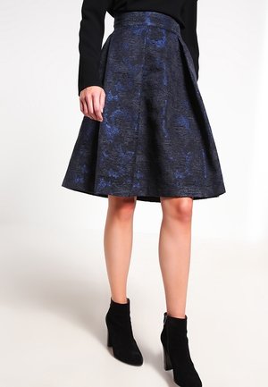 Une jupe évasée jusqu'aux genoux en tissu sombre avec un motif texturé bleu. La taille est plate, associée à des bottines noires.
