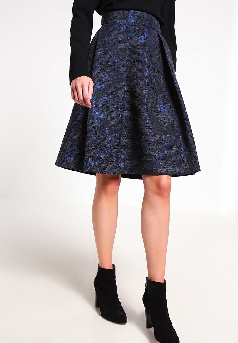 En knälång, utflytande kjol i mörk tyg med ett blått strukturerat mönster. Midjan är platt, och den är kombinerad med svarta ankelstövlar.