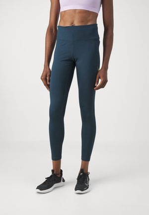 Leggings bleu foncé en matériau extensible, dotés d'une taille haute et d'une texture lisse. Associés à des chaussures de sport noires.
