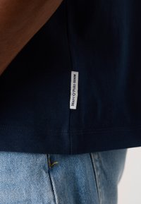 Camiseta de algodón azul marino de manga corta, con dobladillo redondeado y una etiqueta blanca en el lateral que dice "Marc O'Polo DENIM."