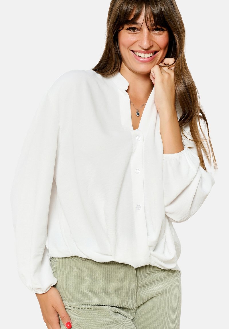 Witte, lichte blouse met een knoopsluiting aan de voorkant, een ontspannen pasvorm en lange mouwen, gecombineerd met olijfgroene geribde broek.
