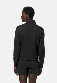 Felpa nera con colletto alto, maniche lunghe e design aderente. Tessuto morbido e dettagli di cucitura visibili. Abbinata a pantaloni corti coordinati.