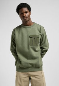 Olijf groene sweatshirt met een ronde hals, een textuurmateriaal en een borstzak met een knoopsluiting. Standaard pasvorm, lange mouwen.