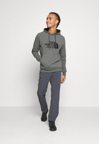 Felpa con cappuccio grigia con logo nero, tasca a marsupio e coulisse, abbinata a pantaloni grigio scuro e stivali neri con lacci.