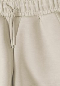 Ceinture beige à cordon sur pantalon ou short en tissu doux avec détails de coutures visibles.