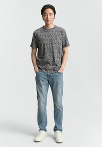 Camiseta gris jaspeada, de manga corta, cuello redondo, combinada con jeans azul claro y zapatillas blancas. Estilo simple, ajuste relajado, sin patrones visibles.