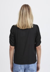 Blusa nera con maniche corte a palloncino, tessuto morbido e vestibilità comoda. Presenta un orlo arrotondato e dettagli minimi.