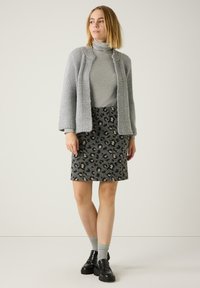 Grauer gestrickter Cardigan über einem grauen Rollkragenpullover, kombiniert mit einem dunklen Leopardenmuster-Rock und schwarzen Loafers. Dezente Texturen und Muster sind sichtbar.