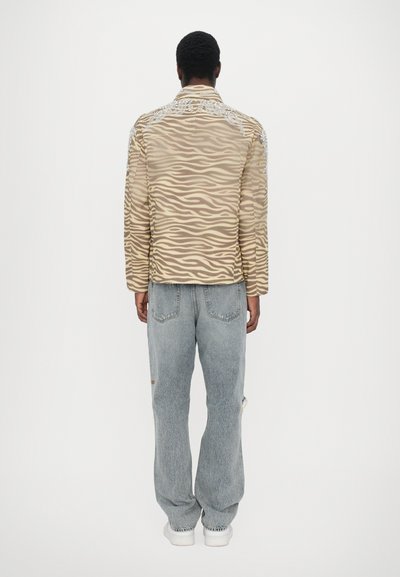 Beige ja pruuni triibuline jakk dekoratiivse mustriga, koos helesiniste denim teksadega. Jakil on krae ja tikandid õlgadel.