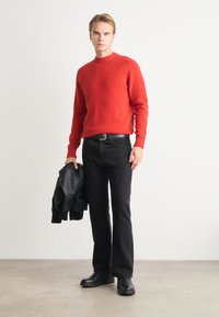 Punane kudum-sweater, millel on ribatud varrukad, koos mustade teksapükstega. Mudel hoiab musta nahktagi. Üksikud värvid, juhuslik sobivus, minimaalne detailitus.