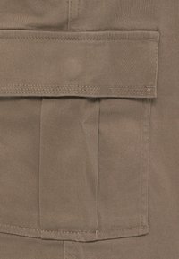 Κοντινή λήψη μπεζ υφασμάτινης τσέπης με καπάκι και ορατή ραφή σε ένδυμα.