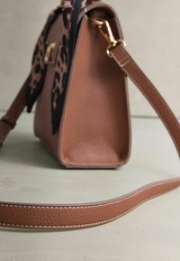 Brązowa skórzana torebka o zorganizowanej konstrukcji, z fakturowaną powierzchnią, odpinanym paskiem oraz dodatkiem w postaci apaszki w leopradowy wzór.