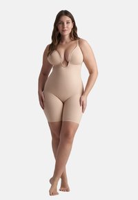 Body in nude con scollo a V profondo e spalline regolabili, caratterizzato da una texture liscia e elastica e lunghezza fino a metà coscia per una copertura senza soluzione di continuità.