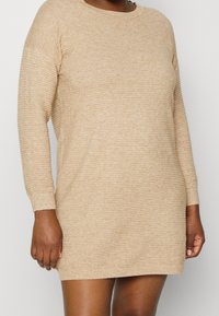 Robe-pull beige en maille avec une texture côtelée, un col rond et des manches longues, à coupe ample avec poignets retroussés.