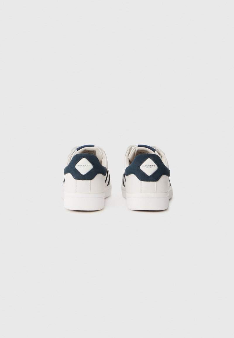 Baskets blanches avec des accents navy, partie supérieure lisse, talon texturé et un patch en forme de diamant à l'arrière. Semelle en caoutchouc, design à lacets.