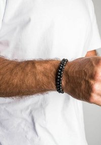 Black bead bracelet featuring smooth and textured stones, worn on a wrist. The beads are alternately sized, showcasing a layered design.