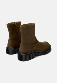 Botines marrones con cremallera en la parte trasera y suela negra gruesa y estriada, mostrados desde la parte trasera sobre un fondo liso.
