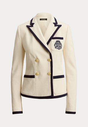 Kremfarget blazer laget av teksturert stoff, med marineblå kanting, gullknapper og en dekorativ brodert logo på brystlommen.