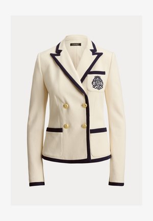 Kremfarget blazer laget av teksturert stoff, med marineblå kanting, gullknapper og en dekorativ brodert logo på brystlommen.