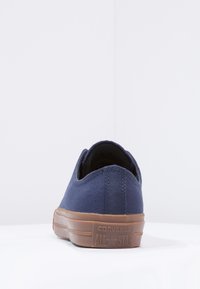 Baskets basses en toile marine avec semelle en caoutchouc, présentant une surface texturée et des accents beige. La vue arrière met en avant le logo "Converse All Star".