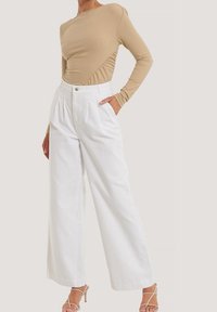 Haut beige à manches longues côtelées associé à un pantalon blanc à jambes larges avec une taille haute et des plis sur le devant. Des sandales à fines lanières complètent le look.