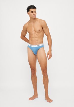 Blaue Baumwollslips mit einem weißen elastischen Bund, der das Logo "POLO RALPH LAUREN" trägt, entworfen für einen engen Sitz, auf einem stehenden Modell.