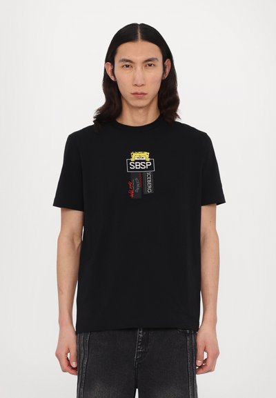 Tricou negru cu mânecă scurtă, prezentând text grafic colorat și logo-uri pe piept. Materialul pare neted, cu un design confortabil.