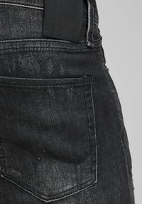Černé džíny z denimu se zadní kapsou s jemnými známkami opotřebení a černou koženou nášivkou označenou "JACK & JONES" poblíž pásku.