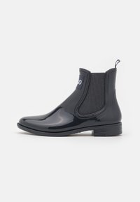 Musta kiiltävä Chelsea-nilkkuri, jossa joustavat sivupaneelit, pyöreä kärki ja pieni palakorko. Varustettu vetonarulla helpottamaan pukemista.