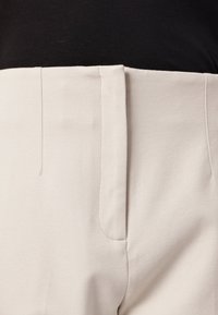 Beige high-waisted pants with a smooth texture, featuring a hidden zipper, vertical seams, and no visible pockets.