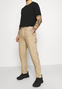 Beiga cargobyxor med sidofickor, rak bendesign och en jämn textur, i samarbete med en svart t-shirt med kort ärm och svarta sneakers.