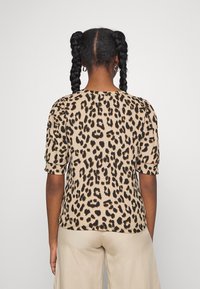 Top s leopardím potiskem v béžové a černé barvě, s krátkými puff rukávy, kulatým výstřihem a strukturovaným designem látky. Klasický střih.