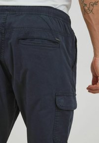 Granatowe spodnie bojówki wykonane z miękkiego materiału, z elastycznym pasem, boczną kieszenią cargo i zapinaną na zamek tylną kieszenią.