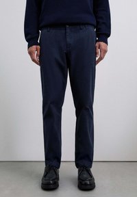 Pantalones de algodón azul marino con pierna recta, con bolsillos laterales y cierre de botón, combinados con zapatos negros de cordones.