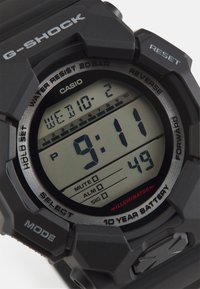 Czarny zegarek G-Shock z wyświetlaczem cyfrowym, dużymi cyframi i różnymi przyciskami funkcyjnymi. Materiał to trwała żywica o teksturowanym wykończeniu.