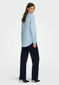 Chemise bleu clair à boutons avec des pois bleu foncé, manches longues, ourlet incurvé. Associée à un pantalon large noir et des talons noirs.