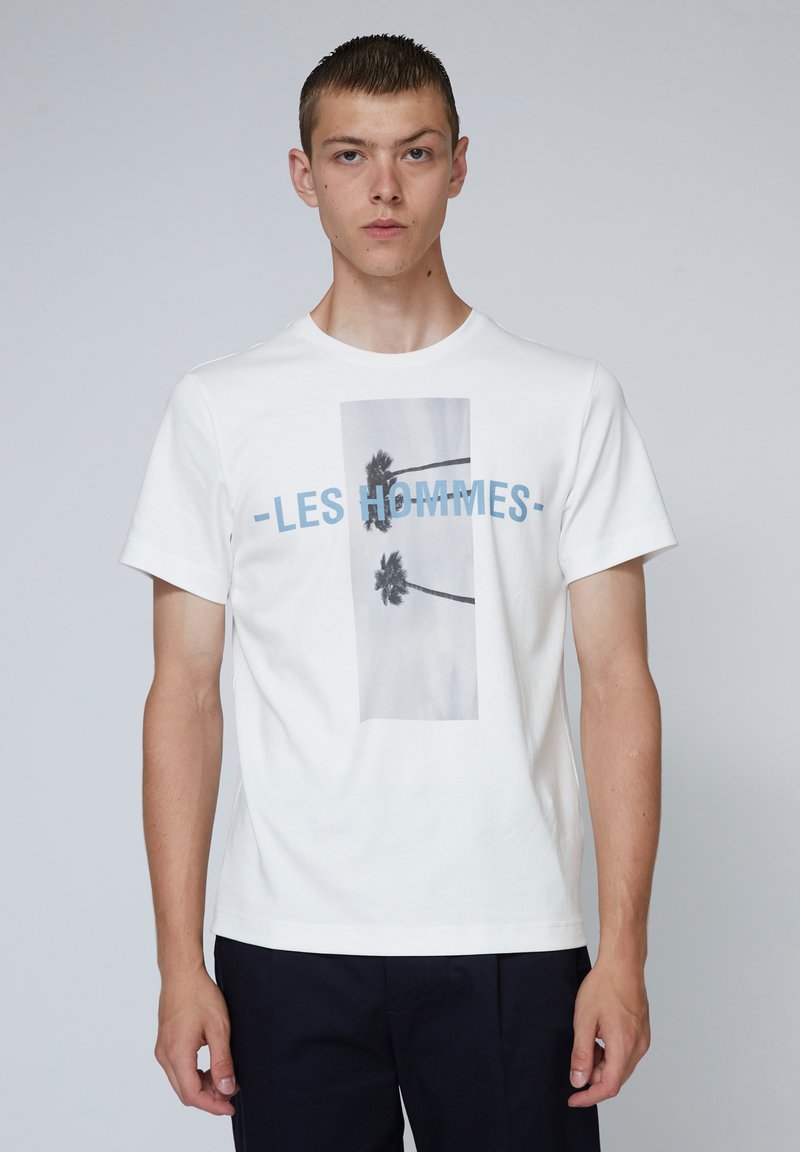 Weißes Baumwoll-T-Shirt mit einem zentralen Grafikmotiv von Palmen und dem Text "LES HOMMES" in Blau. Kurze Ärmel und runder Halsausschnitt.